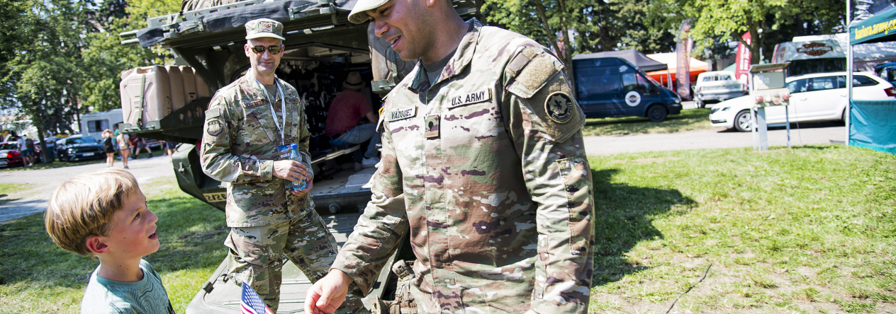 Americký voják předává vlajku USA před obrněným transportérem Stryker
